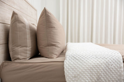 A side view of a bed made with tan zipper bedding with the top unzipped halfway down the bed and the comforter folded down.
