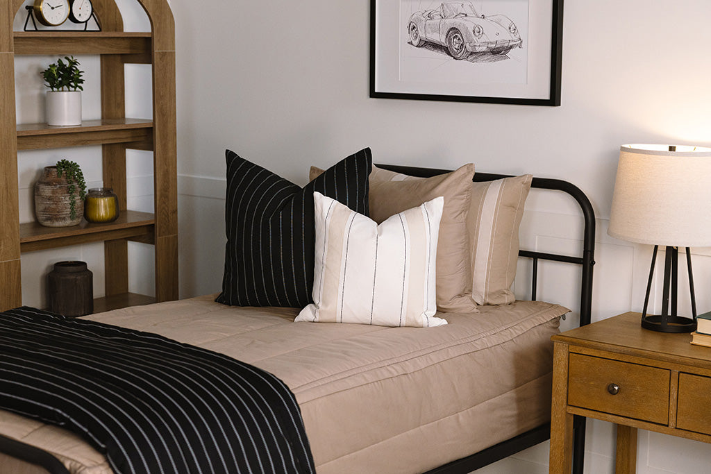 A twin bed made with tan zipper bedding with neutral striped bedding accessories