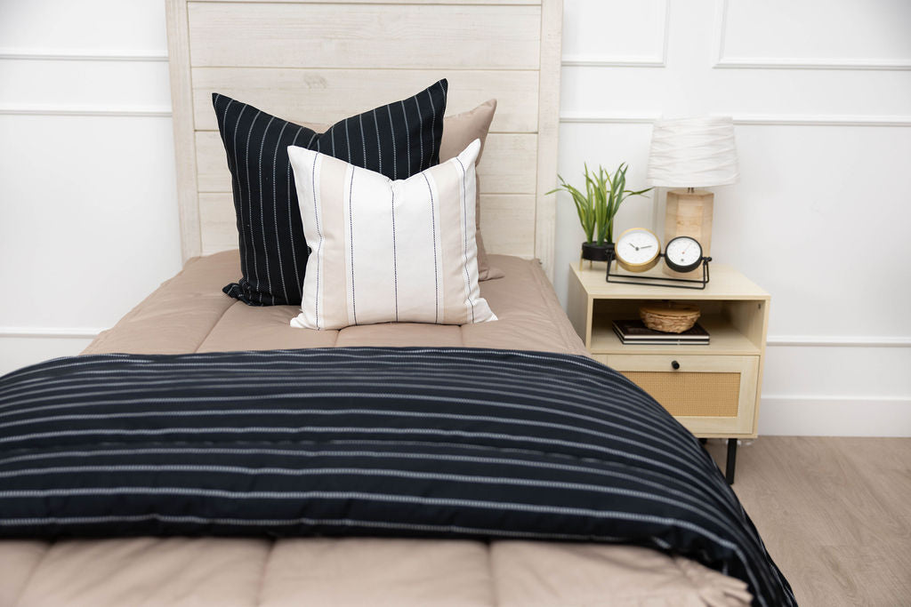 A twin bed made with tan zipper bedding an adorned with neutrals pillows and a matching striped blanket.