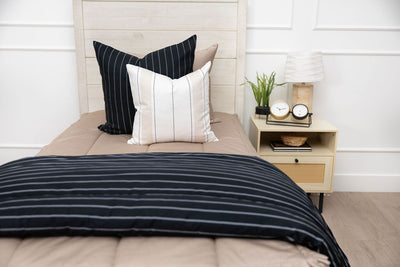 A twin bed made with tan zipper bedding an adorned with neutrals pillows and a matching striped blanket.