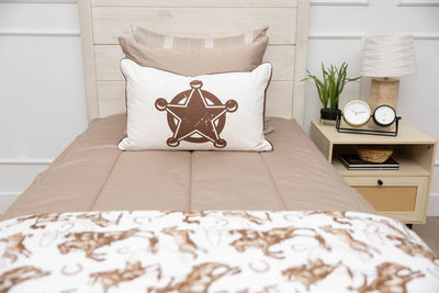 A close up view of a twin bed made with tan zipper bedding and cowboy western printed pillow and blanket.