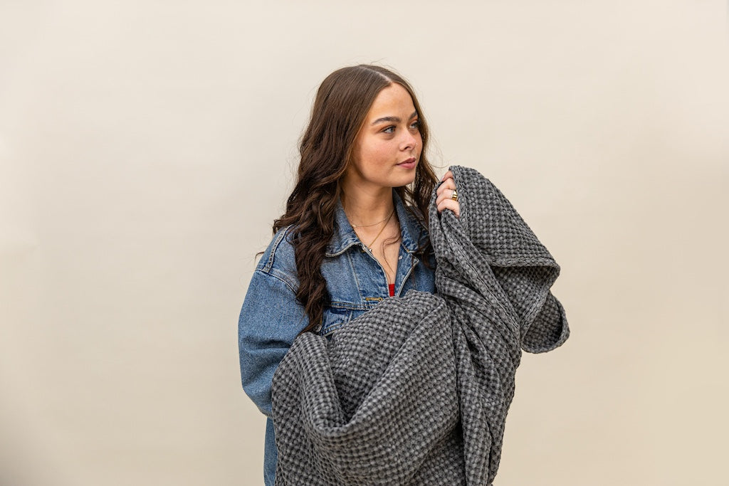 Girl holding a  gray textured waffle weave blanket on a tan background.