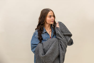 Girl holding a  gray textured waffle weave blanket on a tan background.