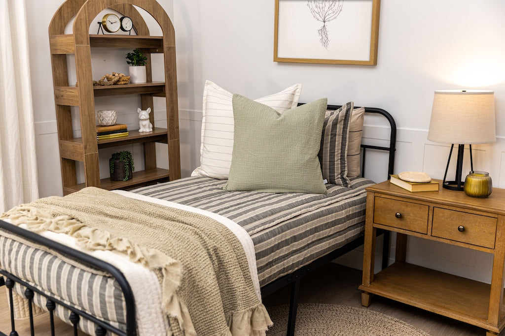 Twin bed with neutral stripe zipper bedding with tan and green accessories.