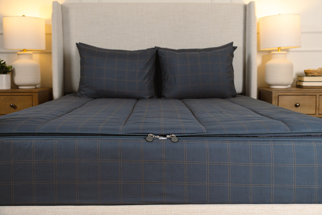 A shot of the two zippers on a set of slate blue grid zipper bedding, the zippers completely unzipped to show how they meet at the foot of the bed. 