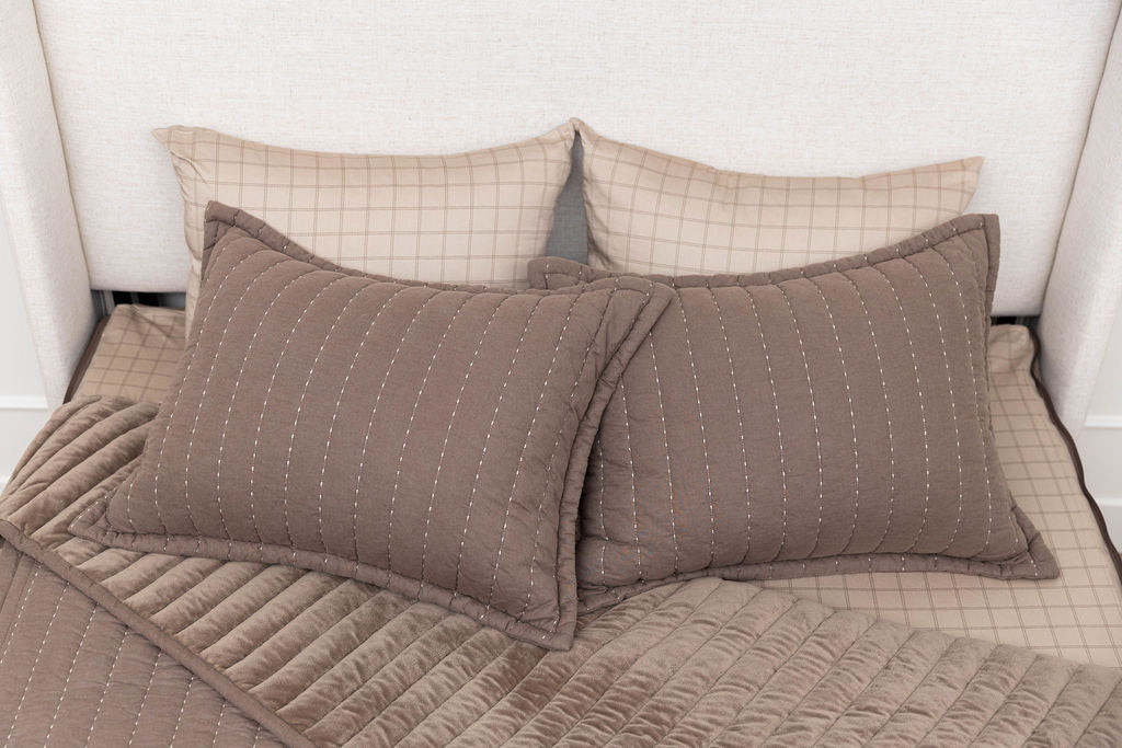 a bed made with brown zipper bedding, the top pulled back to reveal the inside lining and four pillows thrown on top