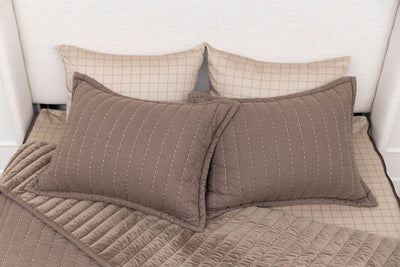 a bed made with brown zipper bedding, the top pulled back to reveal the inside lining and four pillows thrown on top