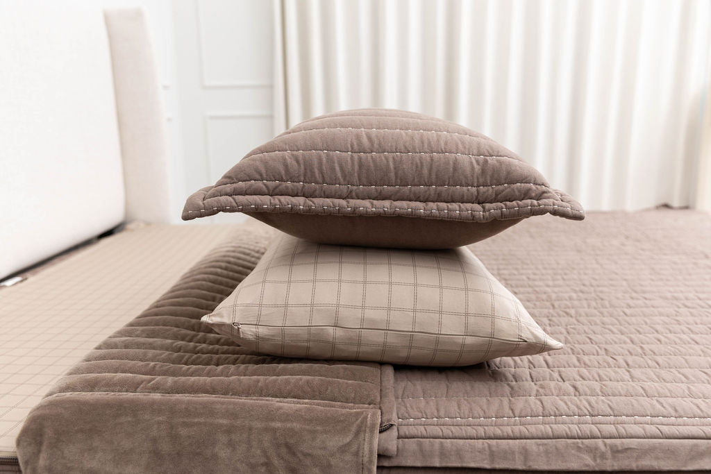 A brown sham stacked on top of a brown grid pillowcase on a bed made with brown zipper bedding