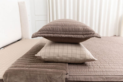 A brown sham stacked on top of a brown grid pillowcase on a bed made with brown zipper bedding