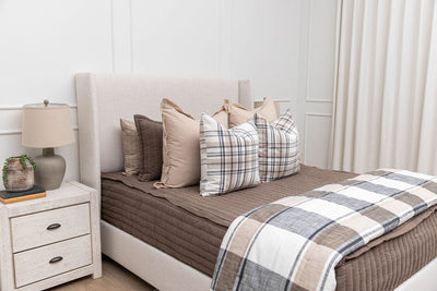 a bed made with brown zipper bedding and an assortment of neutral and plaid bedding accessories