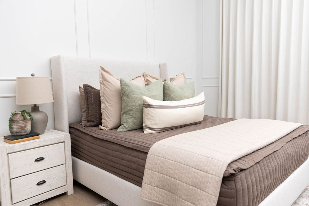 A bed made with brown zipper bedding and a combination of neutral and sage bedding accessories