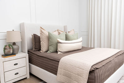 A bed made with brown zipper bedding and a combination of neutral and sage bedding accessories