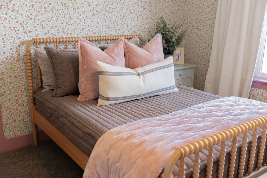A girl's bed made with brown zipper bedding and velvet pink bedding accessories