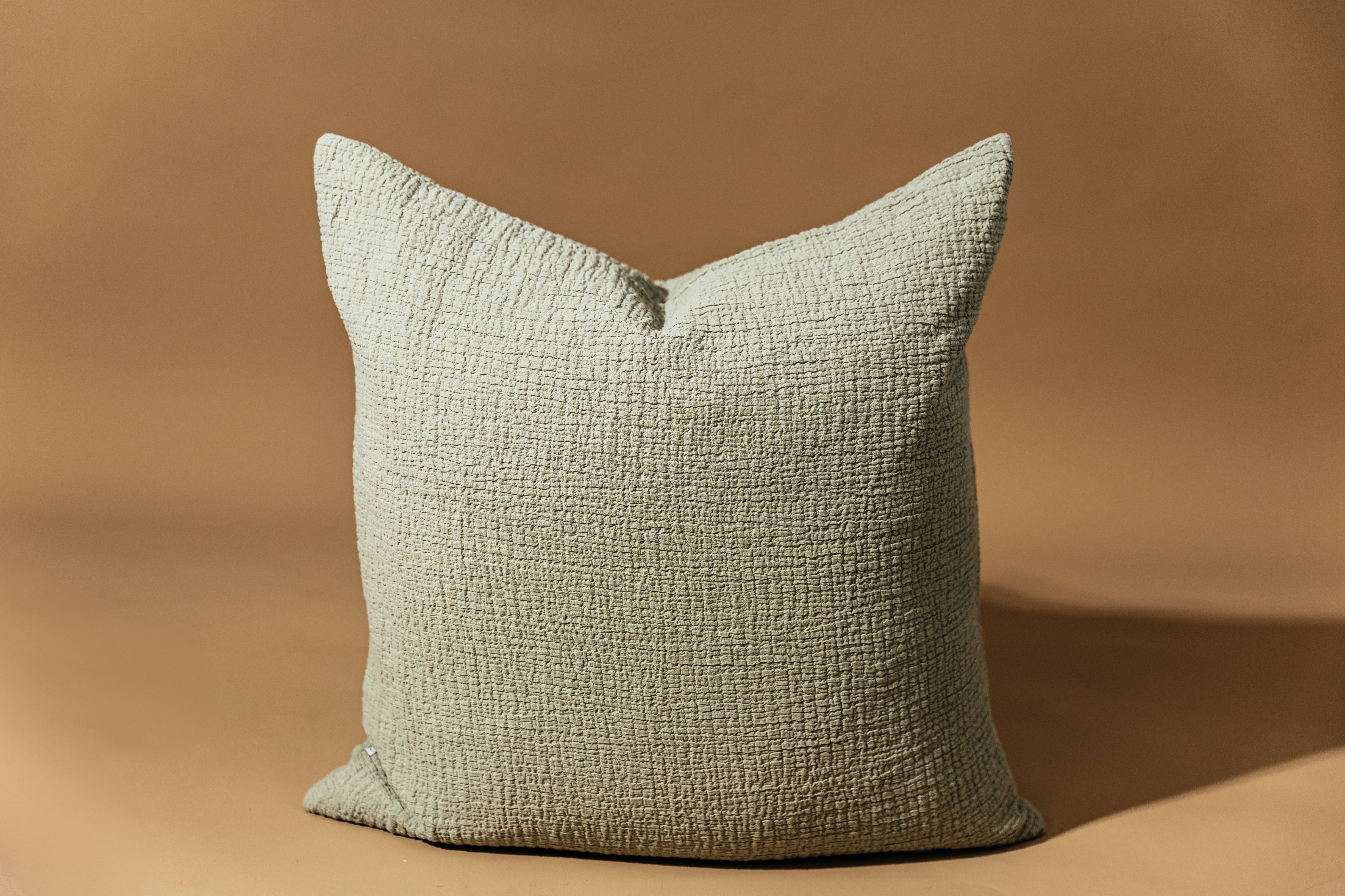 A sage green crinckle textured euro pillow arranged on a brown background.