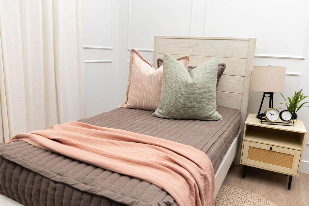 A twin bed made with brown zipper bedding and pink and green bedding accessories