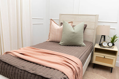 A twin bed made with brown zipper bedding and pink and green bedding accessories