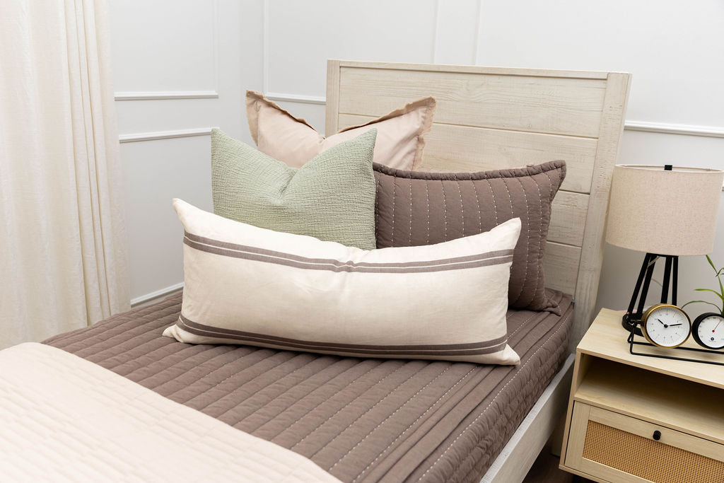 A twin bed made with brown zipper bedding and an assortment of neutral and sage bedding accessorie