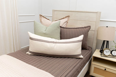 A twin bed made with brown zipper bedding and an assortment of neutral and sage bedding accessorie