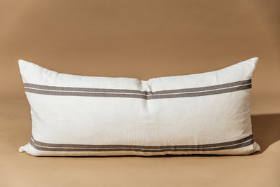 An XL cream lumbar pillow with brown stripes and arranged on a brown background.