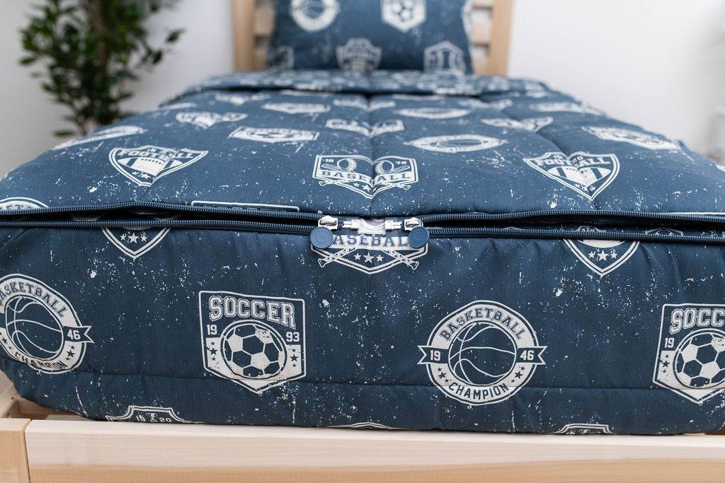 A close up on the foot of a bed made with blue sports themed kids zipper bedding, focusing on the zippers 