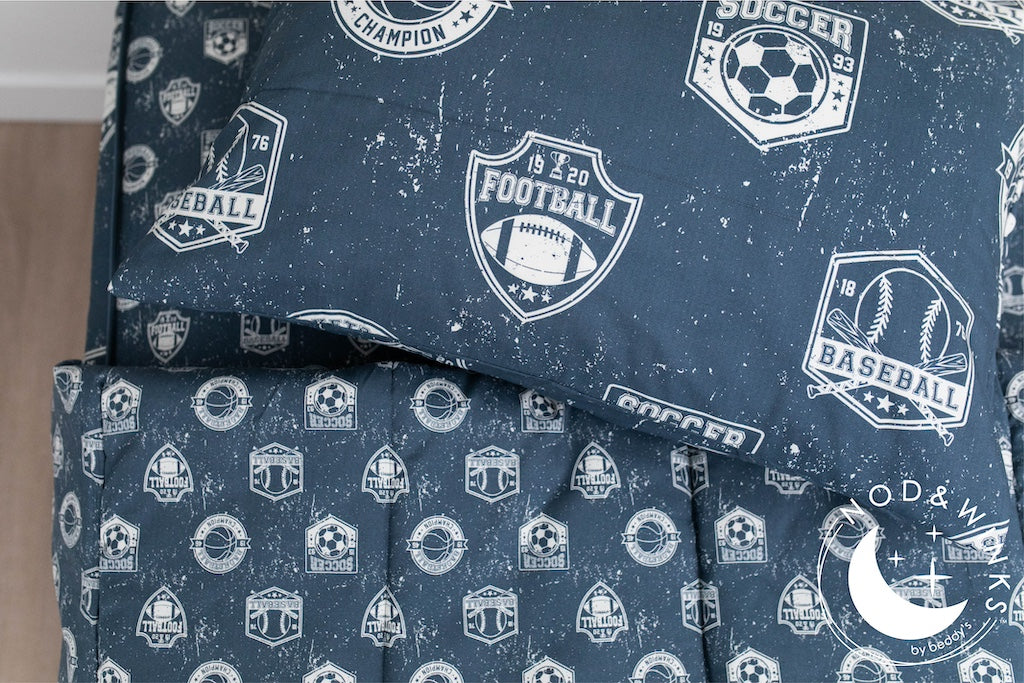 A twin bed made with blue sports themed kids zipper bedding with the top unzipped and pulled back and a pillow on top