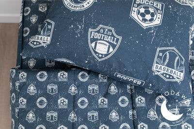 A twin bed made with blue sports themed kids zipper bedding with the top unzipped and pulled back and a pillow on top