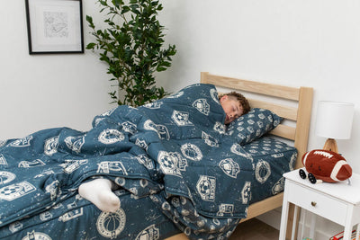 A boy asleep in a twin bed made with blue sports themed kids zipper bedding