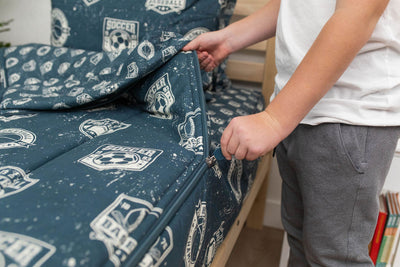 A boy pulling the zipper shut on a set of blue sports themed zipper bedding
