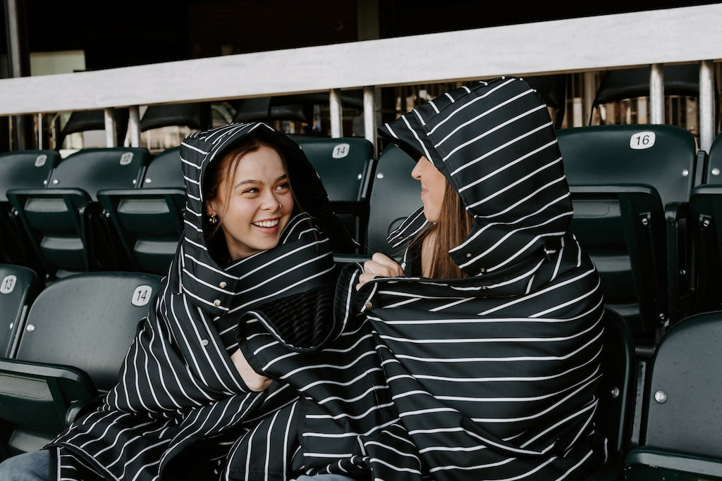 Two women sitting in stadium seating wrapped in stadium water resistant blankets.
