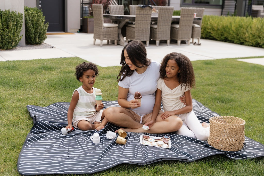 Mother and two kids sitting on a water-resistant blanket outdoors.