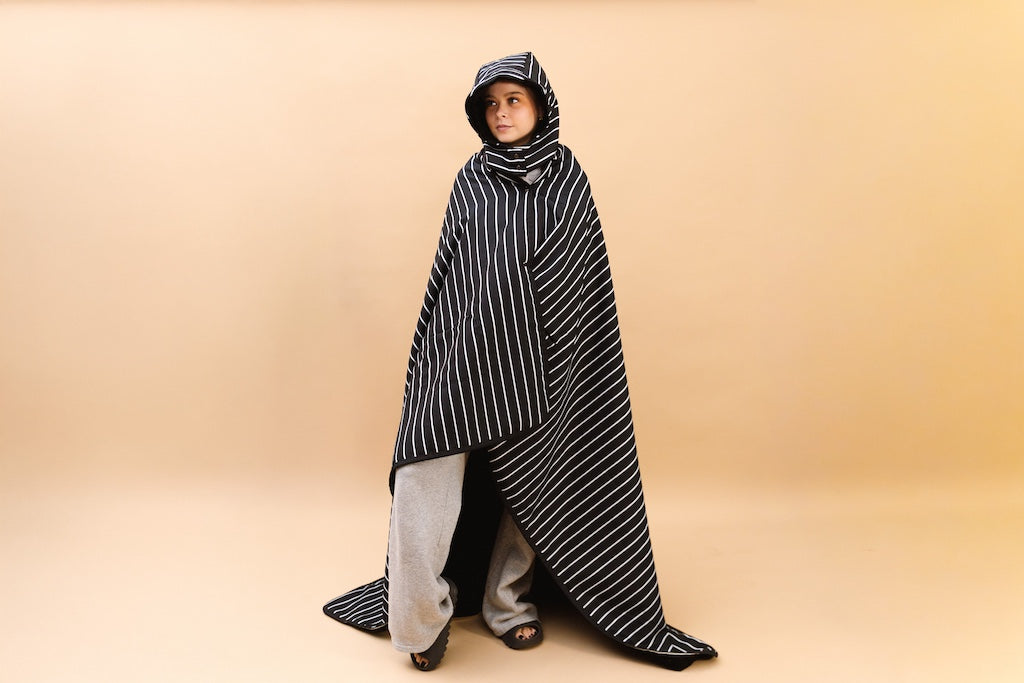 Woman wrapped in the beddy's stadium blanket on a tan background.. 