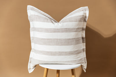A striped neutral pillow on a stool with a brown backdrop behind it