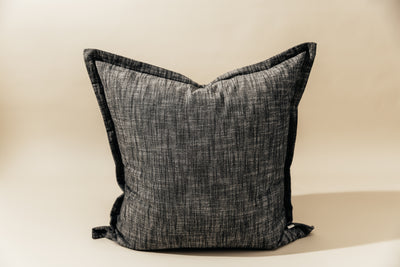 A large charcoal gray pillow on a cream background.