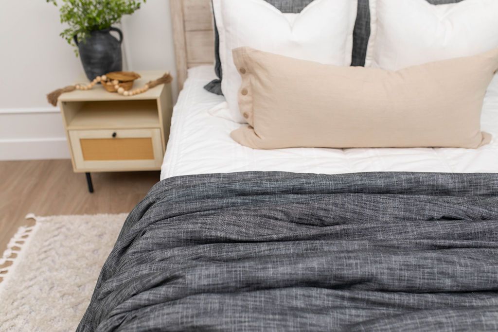 A bed made with white and pinstripes zipper bedding and an assortment of neutral and dark gray pillows and blanket.