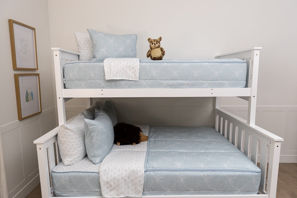 A bunk bed with the top twin and bottom full made with bows printed zipper bedding and stuffed animals on each bed. 