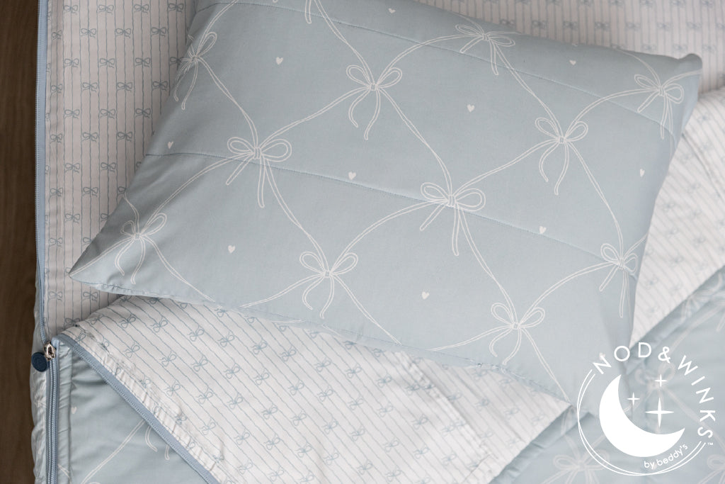 Bows printed kids zipper bedding with the top unzipped and one side pulled back to reveal the inside lining, the pillow tossed on top of the bed.