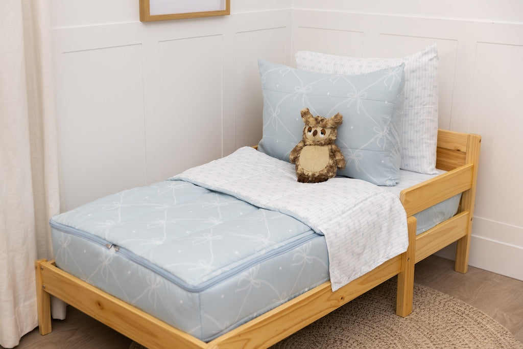 A wooden toddler bed made with bows printed zipper bedding and a stuffed animal leaning against the pillows.
