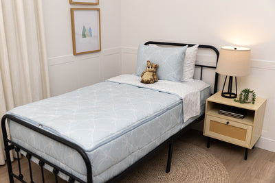 A twin bed made with bows zipper bedding, a nightstand beside the bed and a stuffed animal propped up against the pillow.