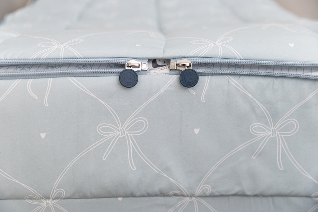 A shot of the two zippers on a set of bows printed zipper bedding, the zippers completely unzipped to show how they meet at the foot of the bed.