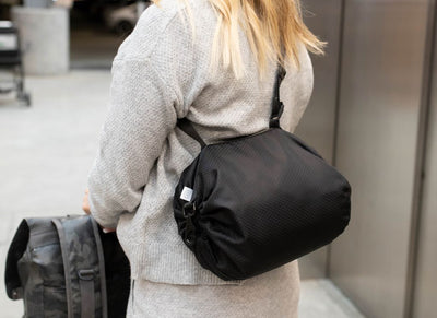 A person with their luggage walking in an airport and a close up view of a black rounded bag strapped to them. 