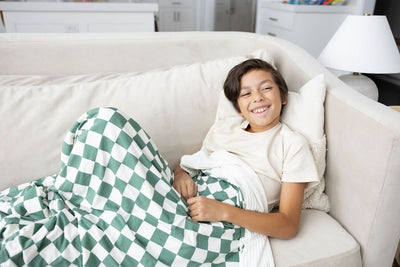 A child on a couch with a green and white checkered print blanket on them. 