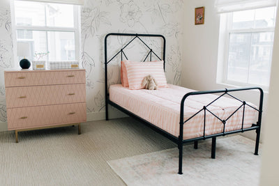 A twin bed made with pink ballet shoes kids zipper bedding with a black bed frame and a pink dresser next to it.
