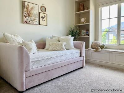 A pink velvet daybed made with white woven plaid zipper bedding and an assortment of neutral pattern throw pillows.