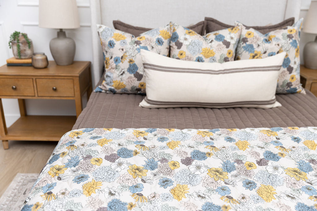 A bed made with brown zipper bedding and blue and yellow floral bedding accessories