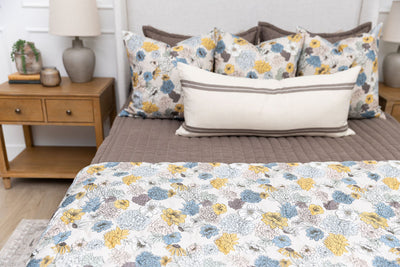 A bed made with brown zipper bedding and blue and yellow floral bedding accessories