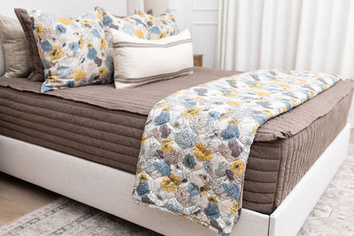 A bed made with brown zipper bedding and blue and yellow floral bedding accessories