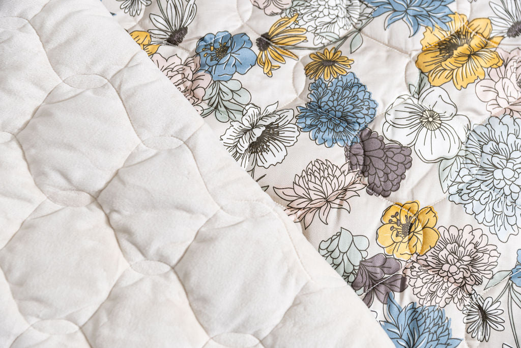 A dual sided blanket, one with a blue and yellow floral print and the other with cream minky