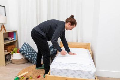 A mom wiping the top of an absorbant ed pad that is sitting on her child's toddler bed