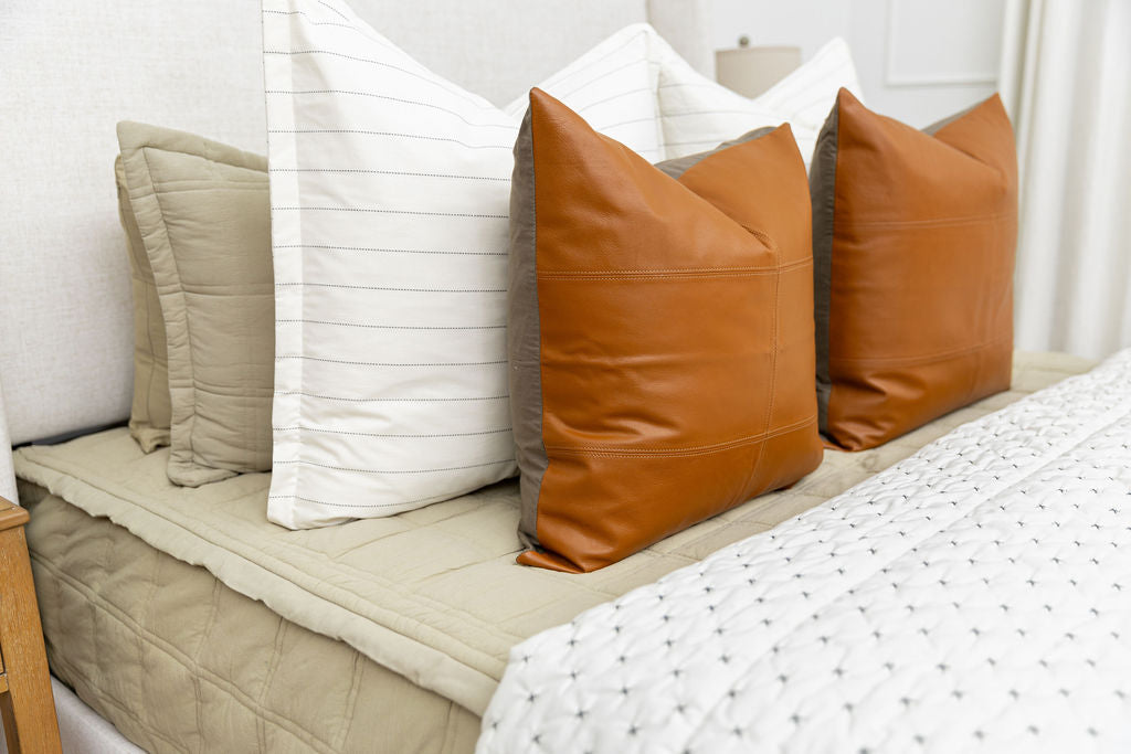 A bed made with green zipper bedding with an assortment of cream and leather bedding accessories