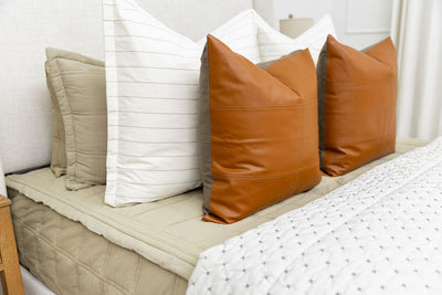 A bed made with green zipper bedding with an assortment of cream and leather bedding accessories